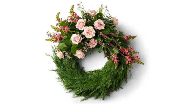 En klassisk krans med rosa rosor tillsammans med blandade blommor i samma färgskala på en cypresstomme.