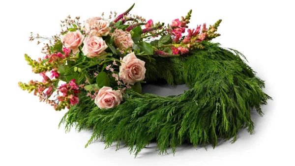 En klassisk krans med rosa rosor tillsammans med blandade blommor i samma färgskala på en cypresstomme.